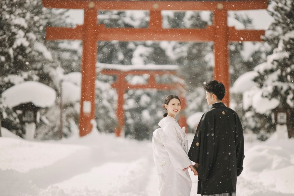雪の北海道護國神社の朱色の鳥居の前に立つふたり