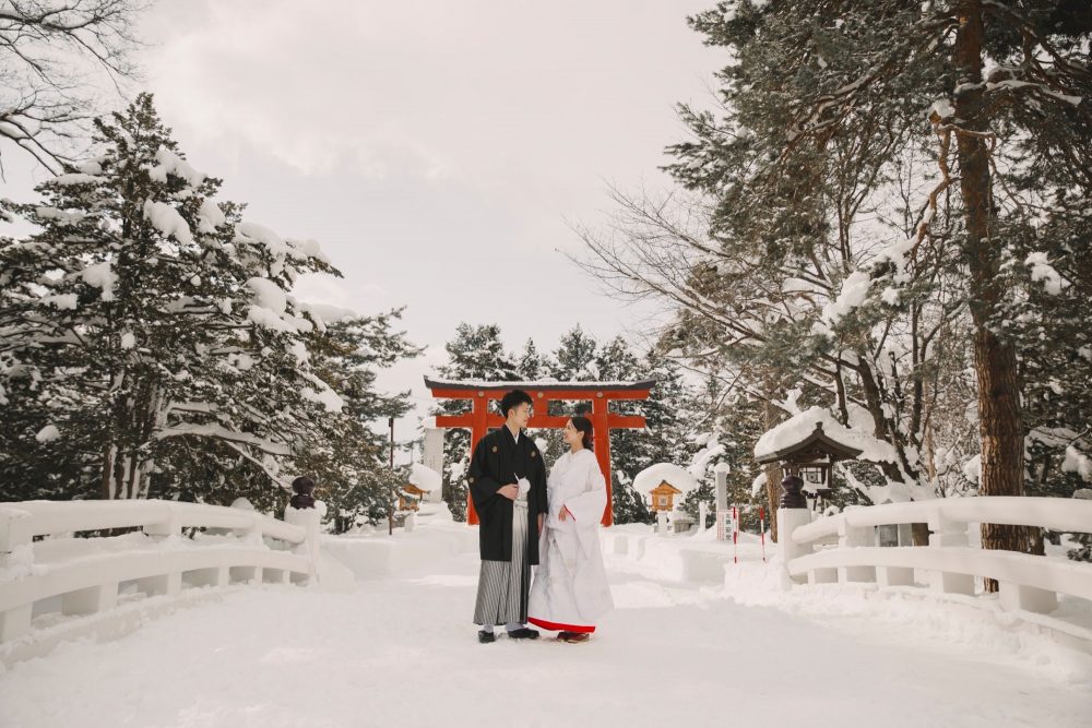 雪の参道で鳥居を背に並ぶふたり(北海道護國神社)