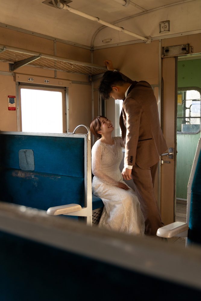 列車の座席に座る花嫁と、そばに立って見つめる新郎(幸福駅)