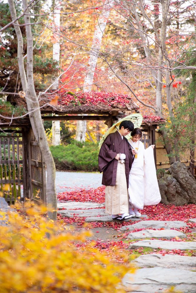 紅葉に囲まれた真鍋庭園の門の前に立つ和装のふたり