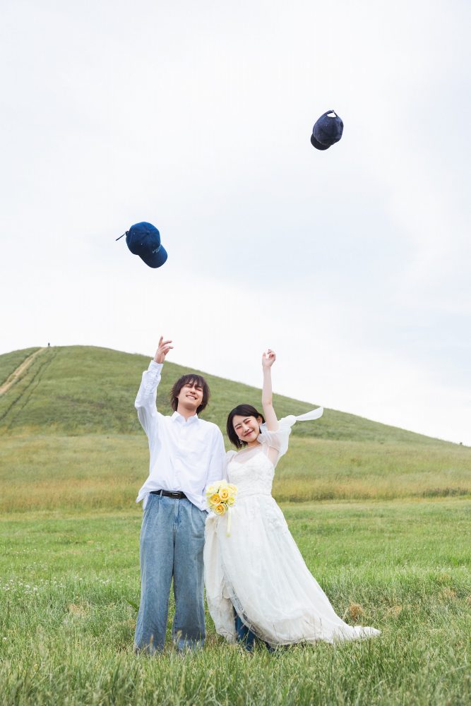 モエレ山を背に帽子を投げ上げるふたり