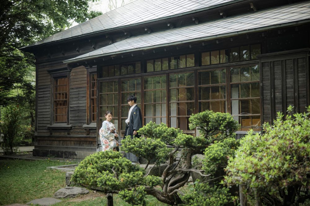 旧永山邸の建物と庭を背景に並ぶ和装のふたり